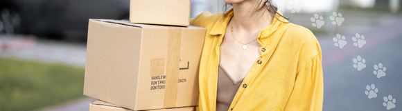 A woman in a brown tank top with a yellow shirt layered over it, holding at least three stacked boxes.